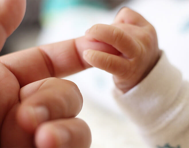 Baby holding adult finger closely