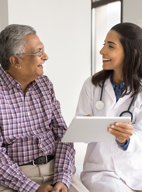 A doctor holds a tablet computer and discusses medical care options with a patient